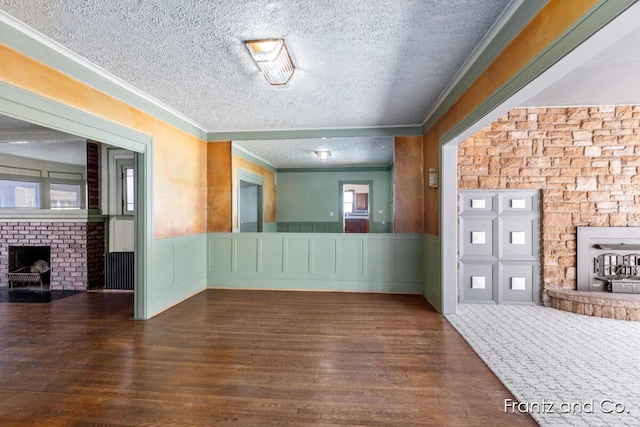 interior space with ornamental molding, wainscoting, a fireplace, wood finished floors, and a textured ceiling