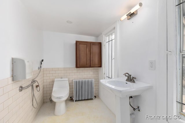 bathroom featuring wainscoting, radiator, toilet, and tile walls