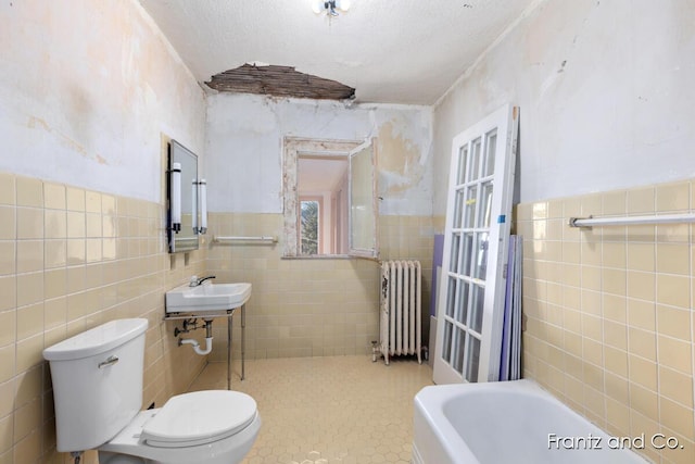 full bath featuring toilet, tile walls, radiator heating unit, and a textured ceiling