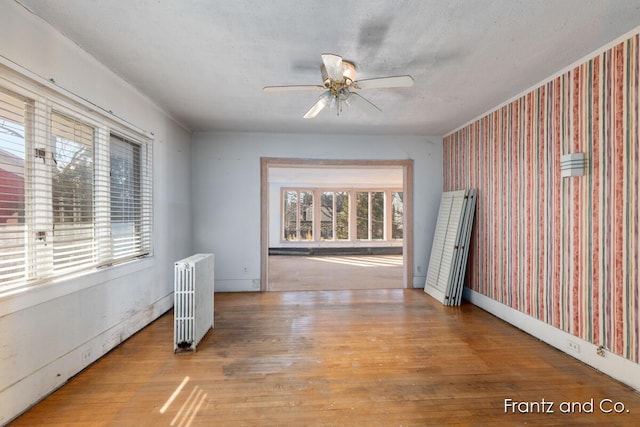 spare room featuring wallpapered walls, ceiling fan, baseboards, radiator heating unit, and wood finished floors