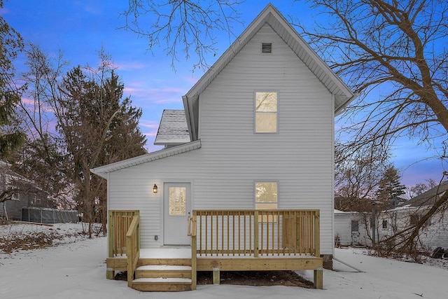 snow covered rear of property with roof with shingles and a wooden deck