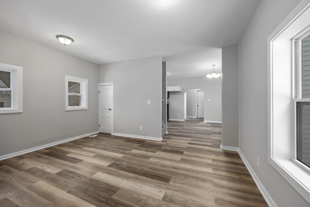 spare room featuring arched walkways, a notable chandelier, baseboards, and wood finished floors