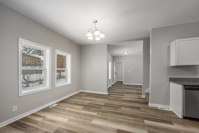 unfurnished dining area with an inviting chandelier, light wood-style flooring, visible vents, and baseboards