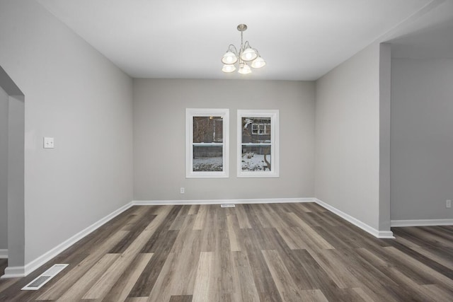 unfurnished dining area featuring an inviting chandelier, wood finished floors, visible vents, and baseboards