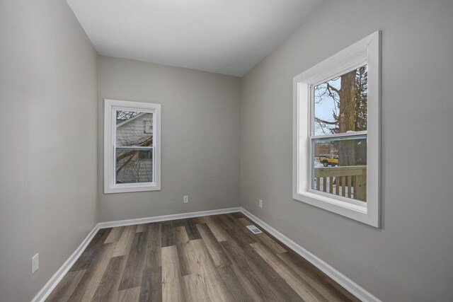 empty room with dark wood-type flooring, visible vents, and baseboards