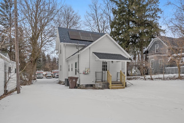 view of front of home with a shingled roof, cooling unit, and solar panels