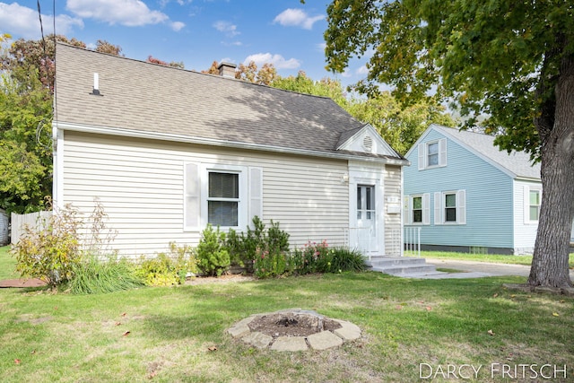 view of front facade featuring a front lawn, an outdoor fire pit, roof with shingles, and a chimney