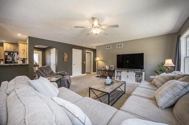 living room with arched walkways, visible vents, light colored carpet, and ceiling fan