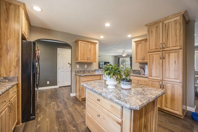 kitchen featuring a kitchen island, dark wood finished floors, freestanding refrigerator, arched walkways, and baseboards