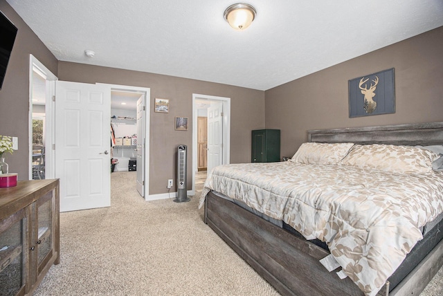 bedroom featuring a walk in closet, baseboards, light colored carpet, and a textured ceiling