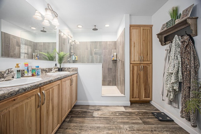 bathroom with wood finished floors, baseboards, double vanity, a sink, and walk in shower