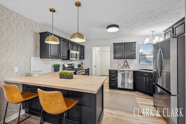 kitchen featuring a peninsula, a sink, stainless steel appliances, light wood-type flooring, and backsplash