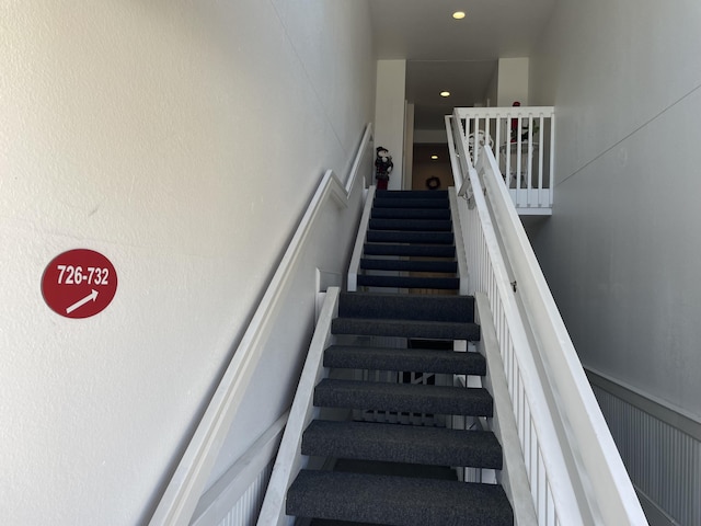 staircase featuring a decorative wall, recessed lighting, and a wainscoted wall