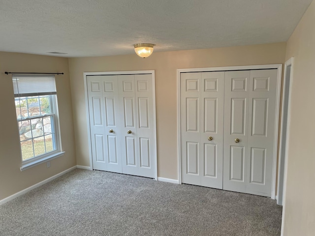unfurnished bedroom with baseboards, a textured ceiling, carpet, and multiple closets