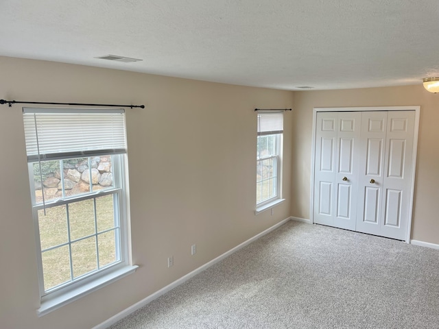 unfurnished bedroom featuring a textured ceiling, carpet, visible vents, and baseboards