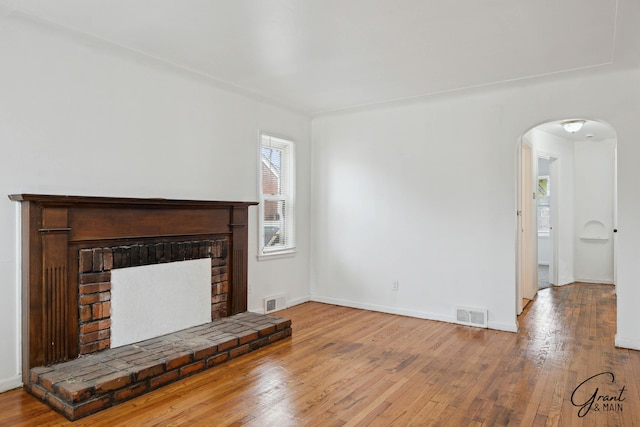 11620 Rossiter St, Detroit, MI 48224 - unfurnished living room with arched walkways, a brick fireplace, visible vents, and hardwood / wood-style flooring