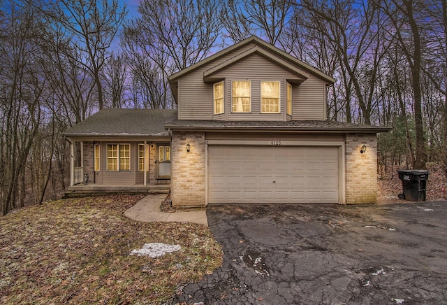 traditional home with covered porch, brick siding, driveway, and an attached garage