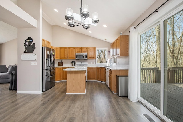 kitchen with a sink, stainless steel appliances, light countertops, a kitchen island, and a notable chandelier
