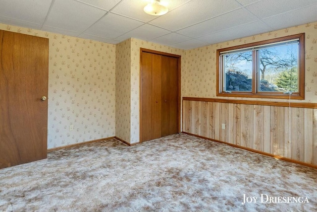 unfurnished bedroom featuring wallpapered walls, a drop ceiling, a closet, and carpet floors