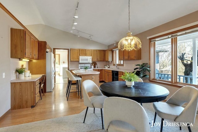 dining room with track lighting, light wood-type flooring, and vaulted ceiling