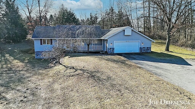 ranch-style home with stone siding, an attached garage, a porch, and driveway