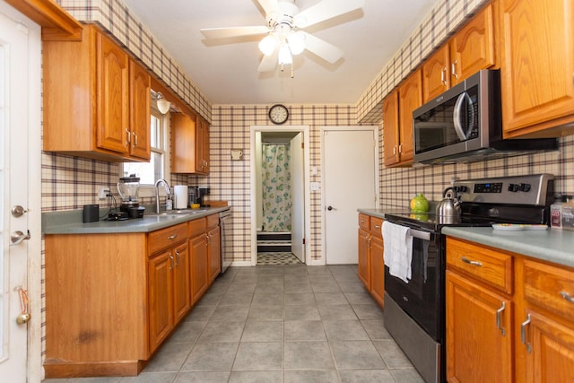 kitchen featuring a sink, appliances with stainless steel finishes, brown cabinetry, light tile patterned floors, and ceiling fan