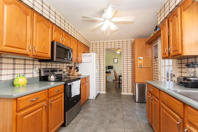 kitchen with brown cabinetry, appliances with stainless steel finishes, a ceiling fan, and dark tile patterned flooring