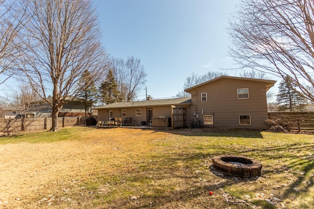 rear view of house with a chimney, an outdoor fire pit, a yard, and fence