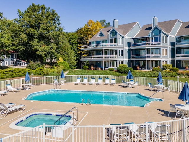 pool with a patio, a community hot tub, and fence