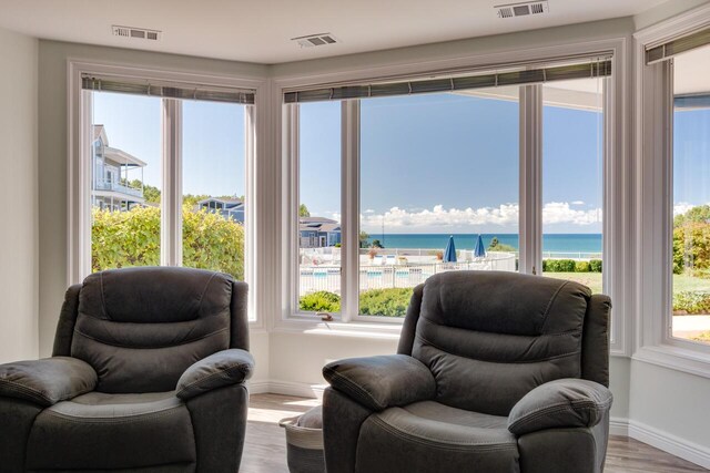 sitting room with a wealth of natural light, visible vents, a water view, and wood finished floors