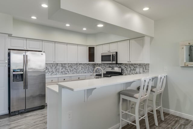 kitchen with backsplash, a breakfast bar, light countertops, a peninsula, and stainless steel appliances