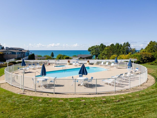 pool featuring a patio, fence, a water view, and a lawn