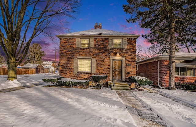 view of front of property featuring brick siding, a chimney, and fence