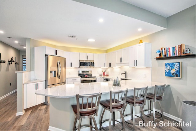 kitchen featuring light stone countertops, decorative backsplash, appliances with stainless steel finishes, a peninsula, and white cabinets