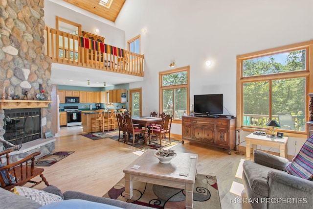 living area featuring light wood finished floors, a skylight, a fireplace, wood ceiling, and a towering ceiling