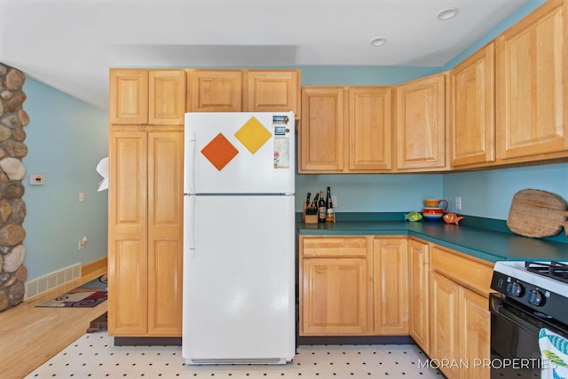 kitchen featuring dark countertops, visible vents, light brown cabinetry, freestanding refrigerator, and gas stove