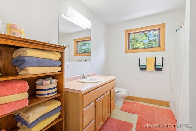 bathroom with baseboards, toilet, a healthy amount of sunlight, and vanity