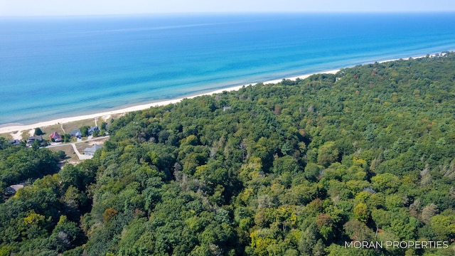 drone / aerial view featuring a wooded view, a view of the beach, and a water view