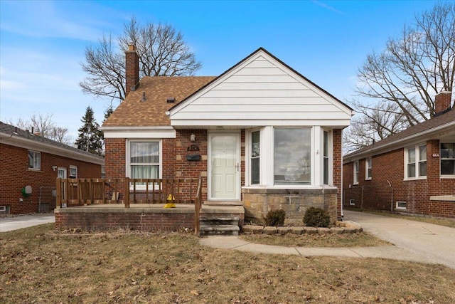 bungalow featuring stone siding, brick siding, roof with shingles, and a chimney