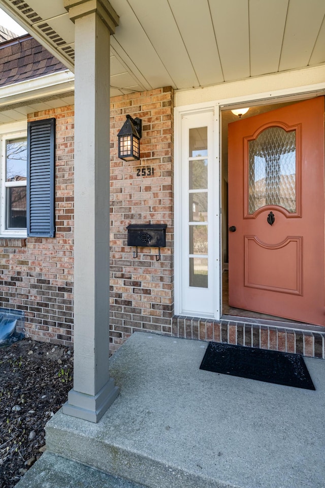 view of exterior entry featuring brick siding and covered porch