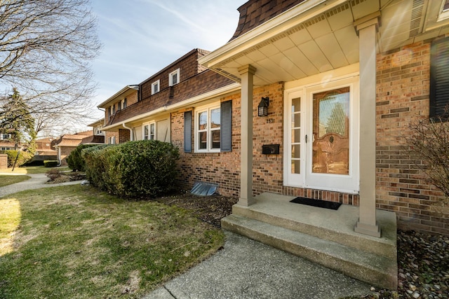 property entrance featuring mansard roof, brick siding, and a shingled roof