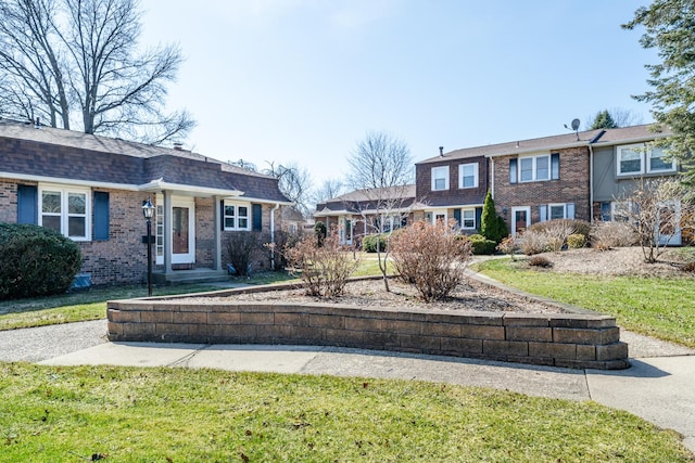 view of front facade featuring brick siding, a front yard, and roof with shingles