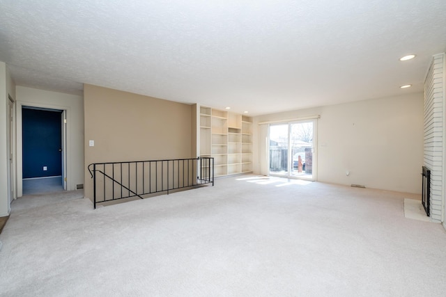 unfurnished room with recessed lighting, light colored carpet, a brick fireplace, and a textured ceiling