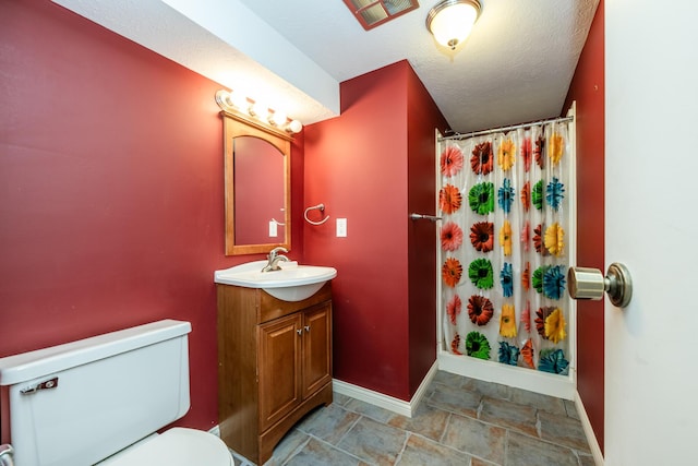 bathroom featuring stone finish flooring, baseboards, toilet, vanity, and a textured ceiling