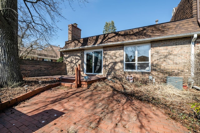 back of property featuring brick siding, fence, roof with shingles, a chimney, and a patio area