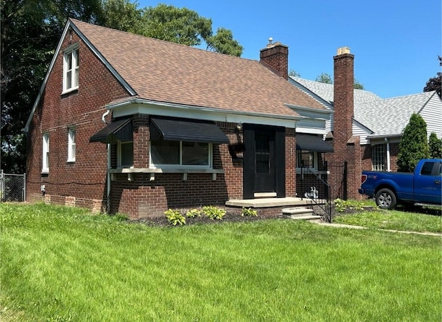 bungalow with fence, brick siding, a front yard, and a shingled roof