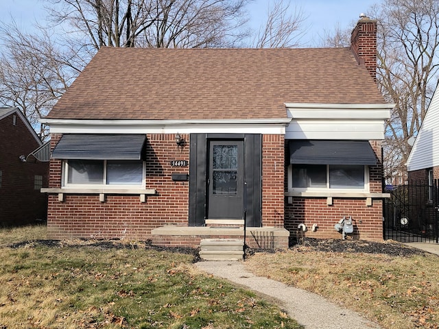 bungalow-style home with brick siding, a chimney, and roof with shingles