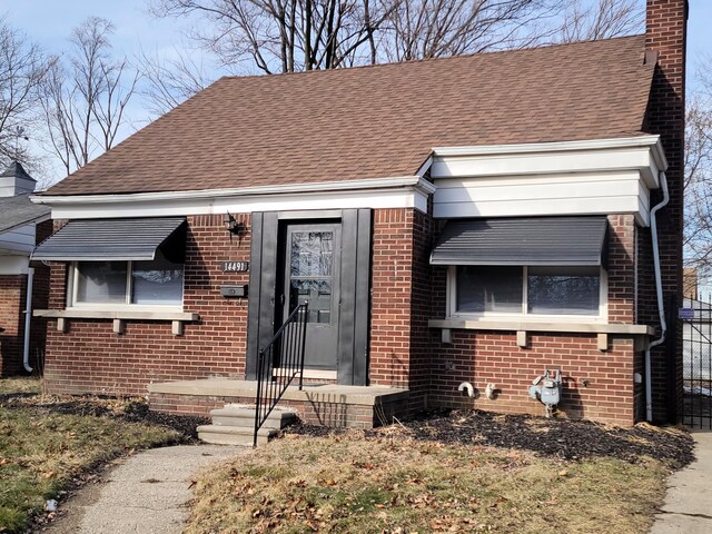 view of front of home featuring brick siding, a chimney, and a shingled roof