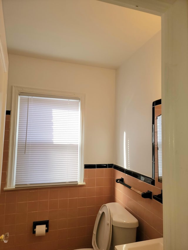 bathroom with a wainscoted wall, toilet, and tile walls