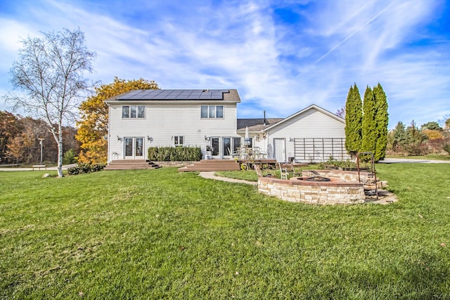 rear view of house featuring a wooden deck, an outdoor fire pit, a yard, french doors, and roof mounted solar panels